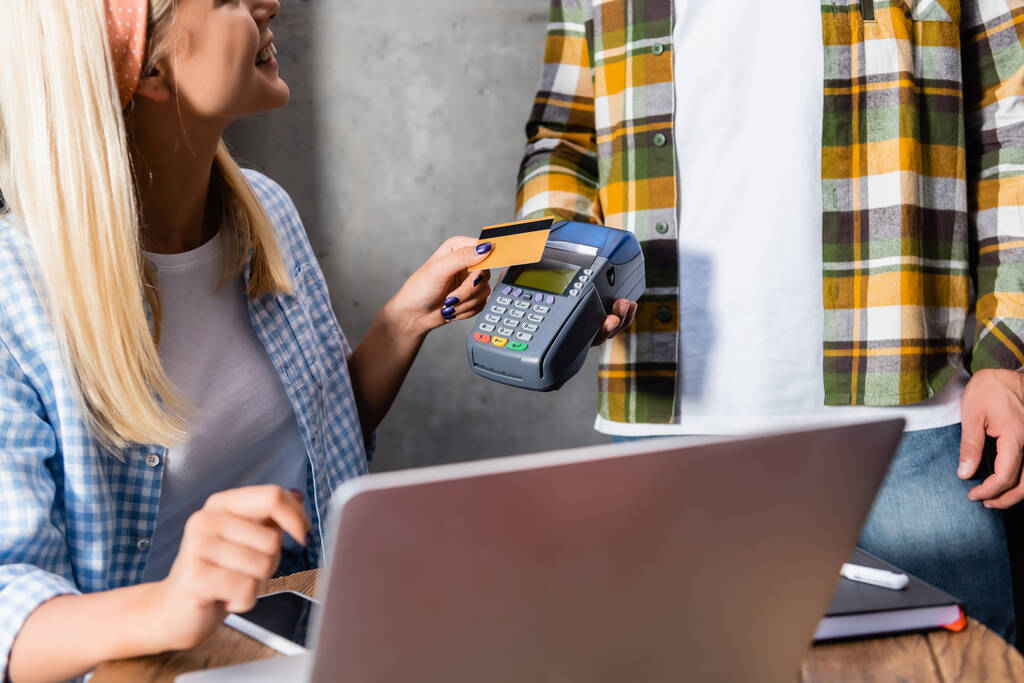 обрезанный вид улыбающегося фрилансера, держащего кредитную карту рядом с официантом с платежным терминалом - Фото, изображение