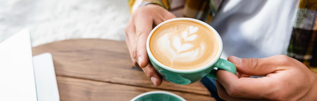 обрезанный вид человека, держащего чашку кофе с латте искусства, баннер - Фото, изображение