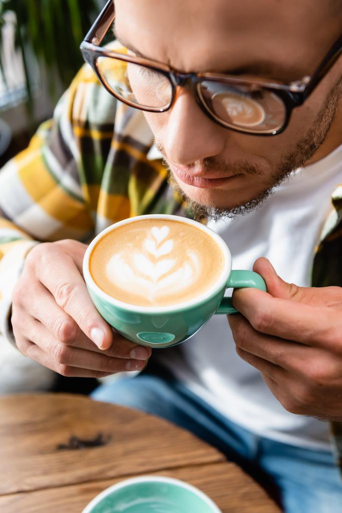 close up view of man in eyeglasses holding cup of coffee with latte art - Photo, Image