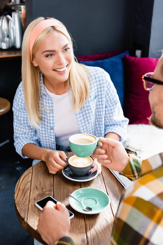 joven sonriente mujer y hombre en primer plano borrosa beber café en la cafetería - Foto, Imagen
