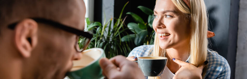 femme gaie tenant tasse près d'un ami boire du café sur le premier plan flou, bannière - Photo, image