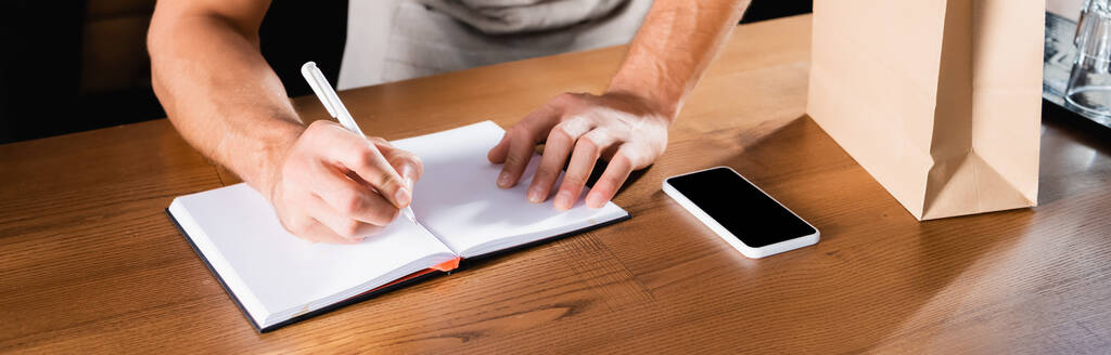částečný pohled na psaní číšníka v notebooku u mobilního telefonu s prázdnou obrazovkou na pultu, banner - Fotografie, Obrázek