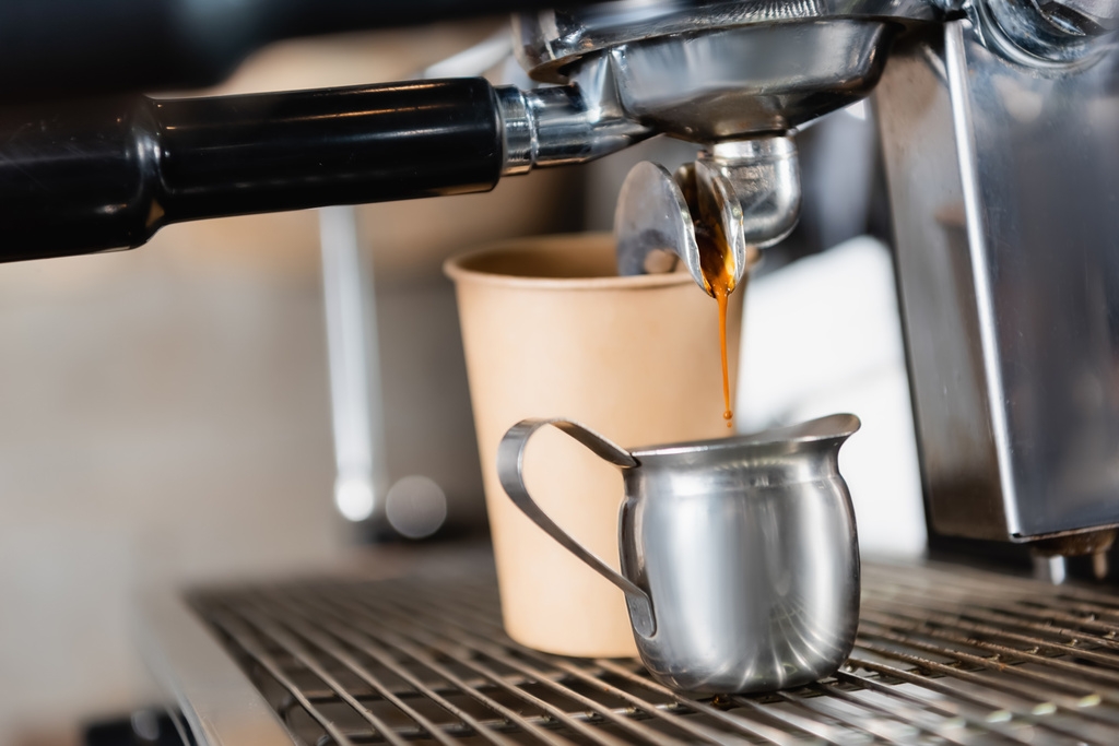 コーヒーマシンディスペンサーの近くの金属製マグカップと背景のぼやけた紙コップ - 写真・画像