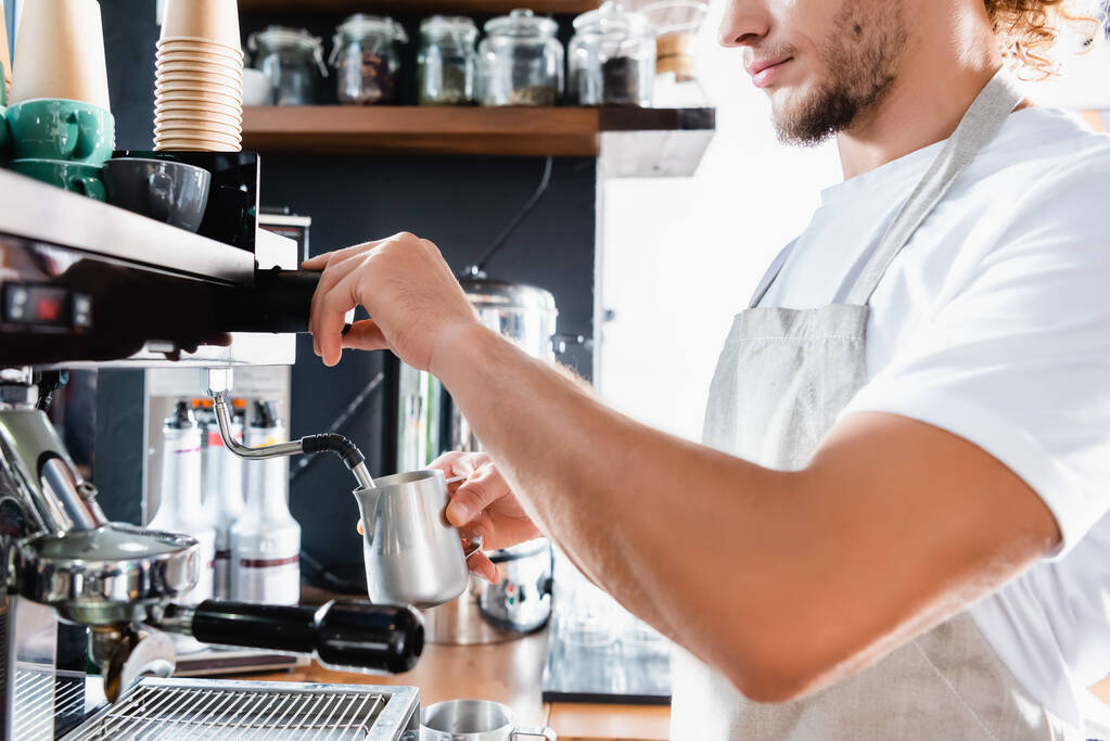 vista parcial de barista em avental segurando caneca de leite perto da máquina de café vapor - Foto, Imagem