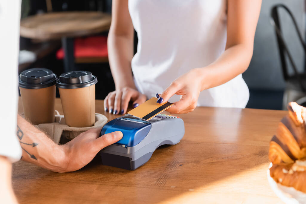 gedeeltelijk zicht op vrouw met kredietkaart in de buurt van barista met betaalterminal op wazige voorgrond - Foto, afbeelding