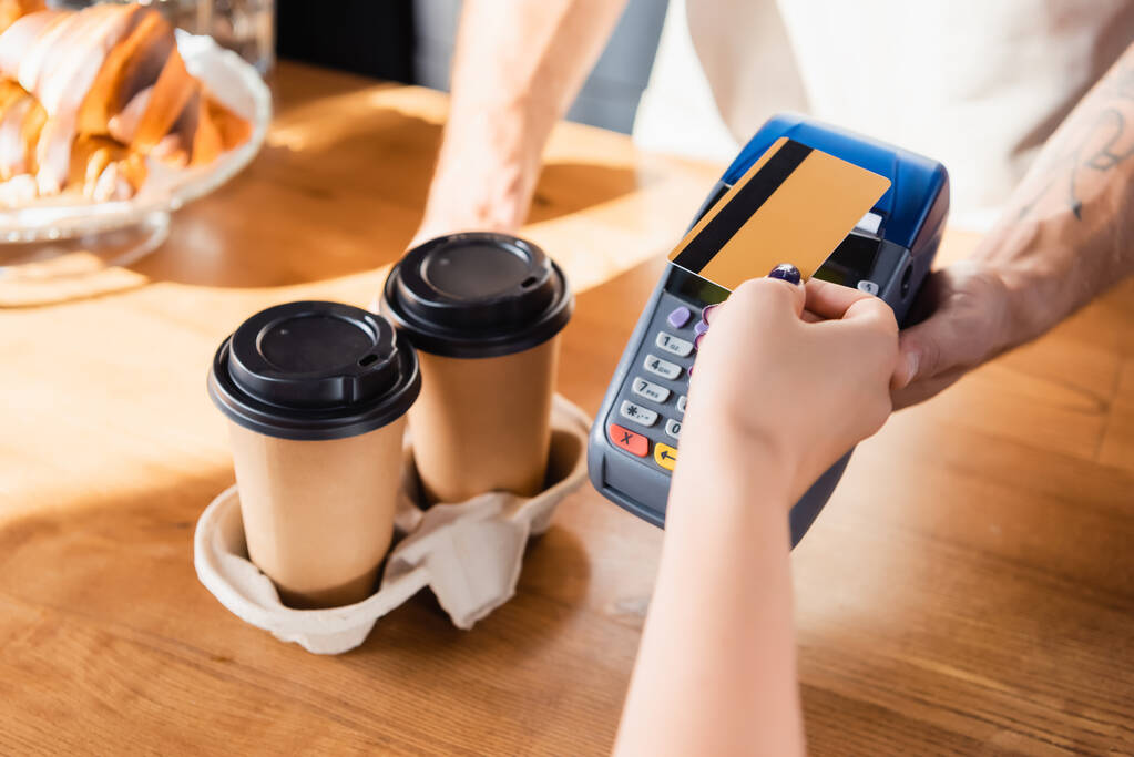 vista parziale di donna in possesso di carta di credito vicino barista con terminale di pagamento su sfondo sfocato - Foto, immagini