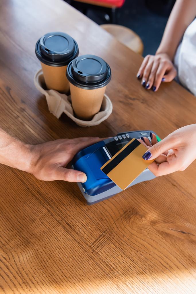 Ausgeschnittener Blick auf Barista mit Zahlungsterminal und Frau mit Kreditkarte in der Nähe von Coffee to go im Café - Foto, Bild