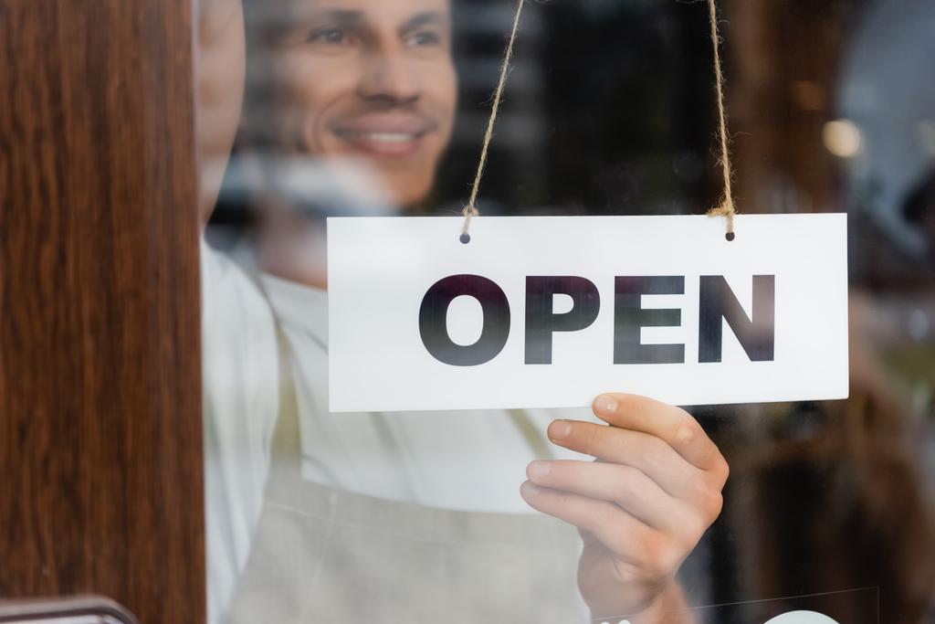 smiling barista hanging card with open lettering on door of cafe entrance - Photo, Image