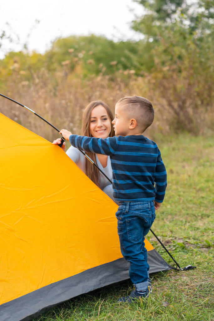 Onnellinen perhe ja pieni poika pystyttivät teltan. Onnellinen lapsuus, telttaretki vanhempien kanssa. Lapsi auttaa pystyttämään teltan.. - Valokuva, kuva