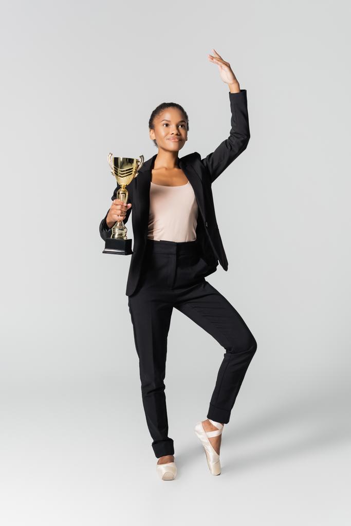 Afrikanisch-amerikanische Geschäftsfrau führt Ballett mit goldener Tasse isoliert auf grau - Foto, Bild