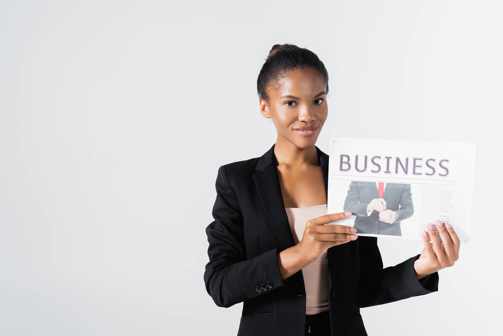 lächelnde afrikanisch-amerikanische Geschäftsfrau mit Wirtschaftszeitung isoliert auf grau - Foto, Bild