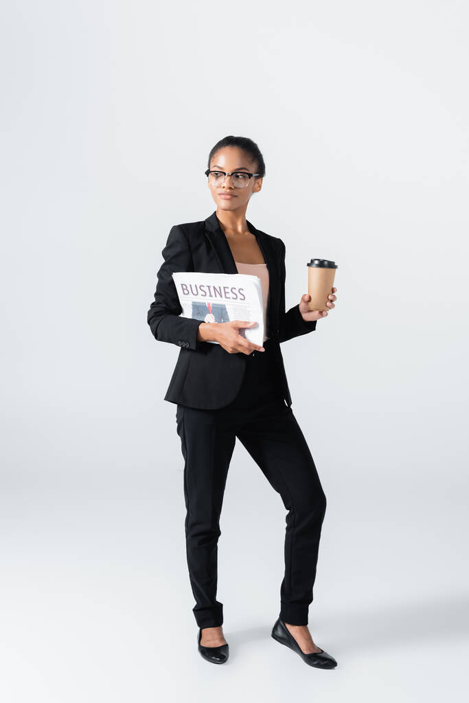 Африканская американская бизнесвумен с бизнес-газеты и кофе, чтобы пойти изолированы на серый - Фото, изображение