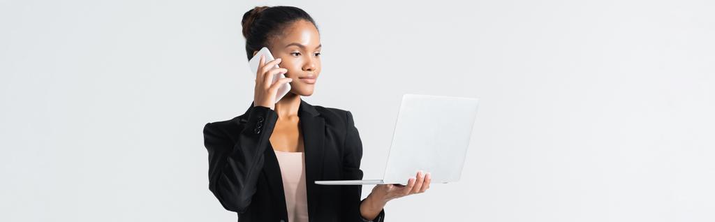 mulher de negócios afro-americana com laptop falando em smartphone isolado em cinza, banner - Foto, Imagem