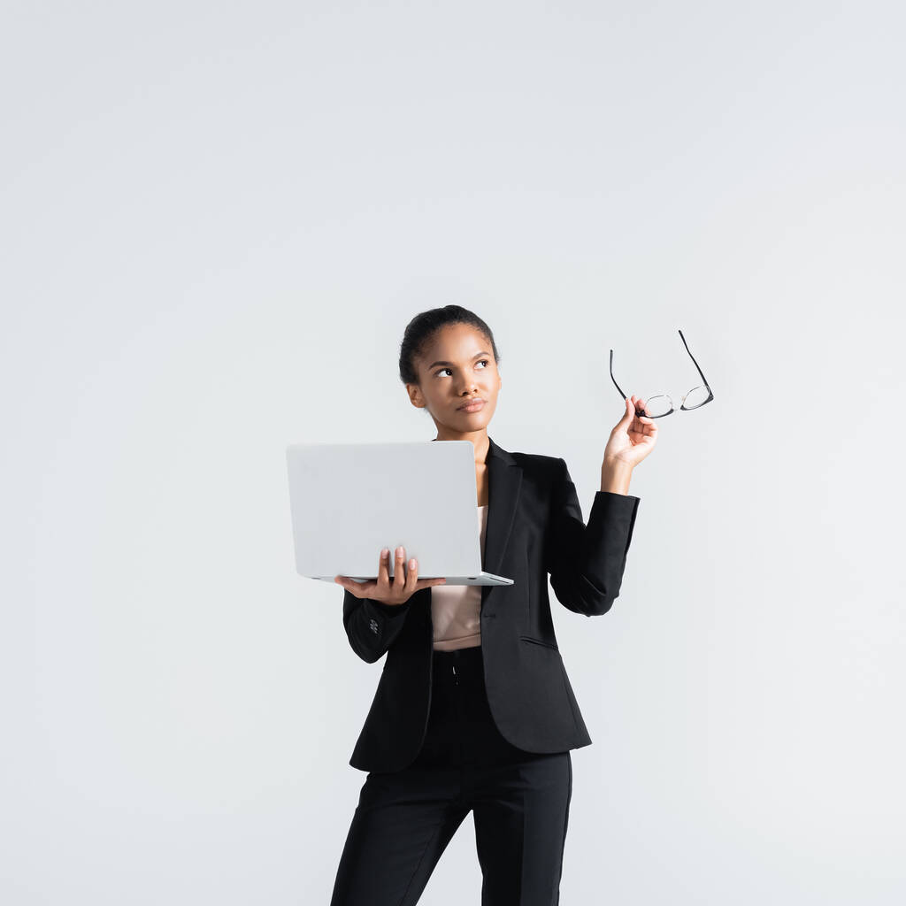 zamyślona afrykańska bizneswoman z okularami i laptopem na szaro - Zdjęcie, obraz