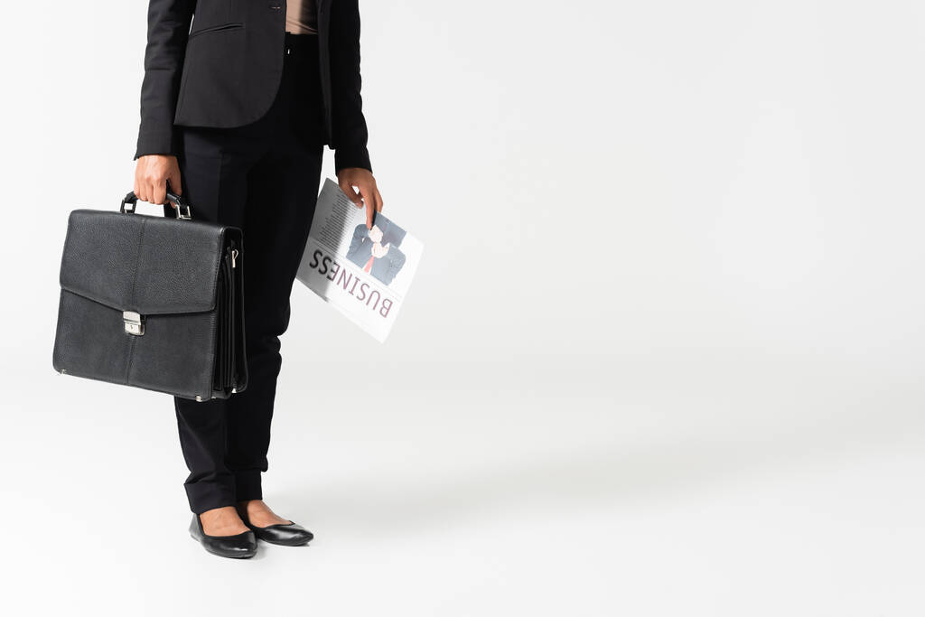 vista ritagliata di donna d'affari afroamericana con valigia e giornale d'affari isolato su grigio - Foto, immagini