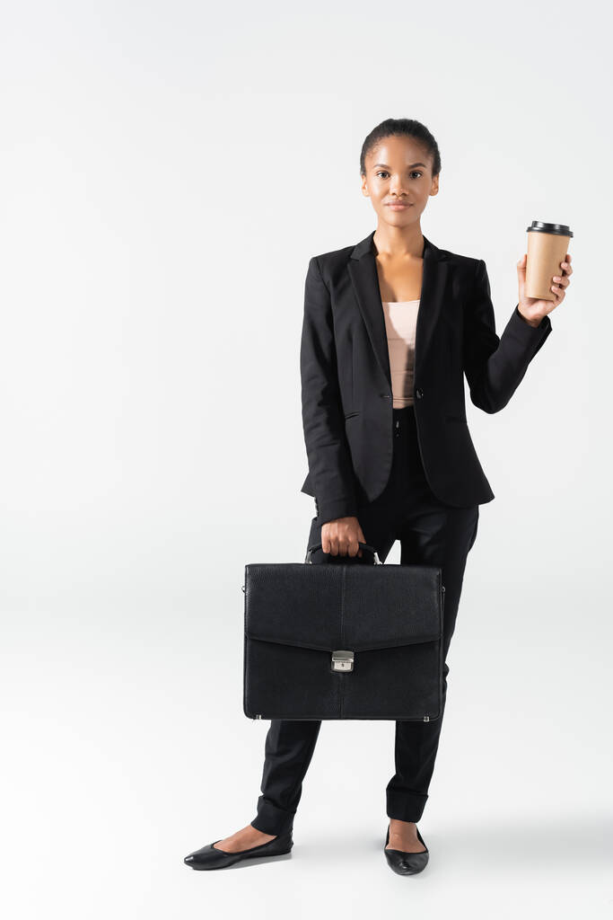mujer de negocios afroamericana con maleta y taza de papel aislada en blanco - Foto, Imagen