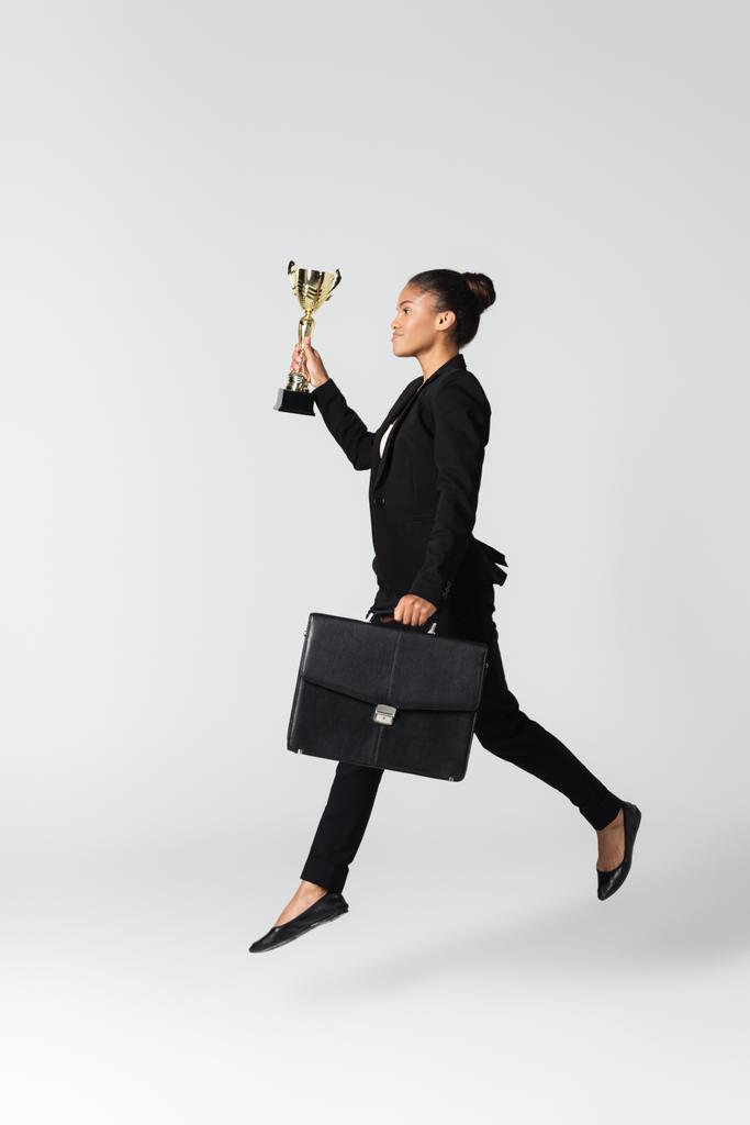 vista lateral de mujer de negocios afroamericana con maleta y copa aislada en blanco - Foto, imagen