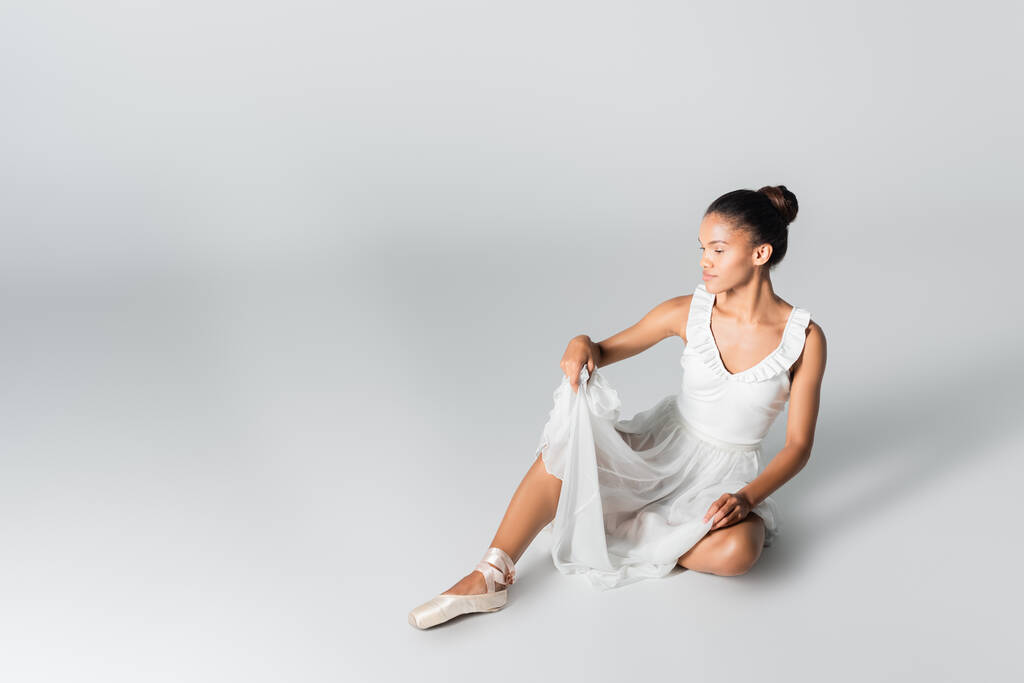 graziosa ballerina afroamericana in abito da ballo sul pavimento su sfondo bianco - Foto, immagini