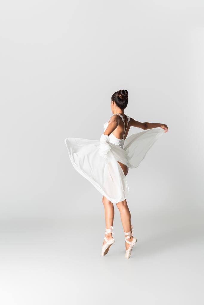 sierlijke Afrikaanse Amerikaanse ballerina in jurk dansen op witte achtergrond - Foto, afbeelding