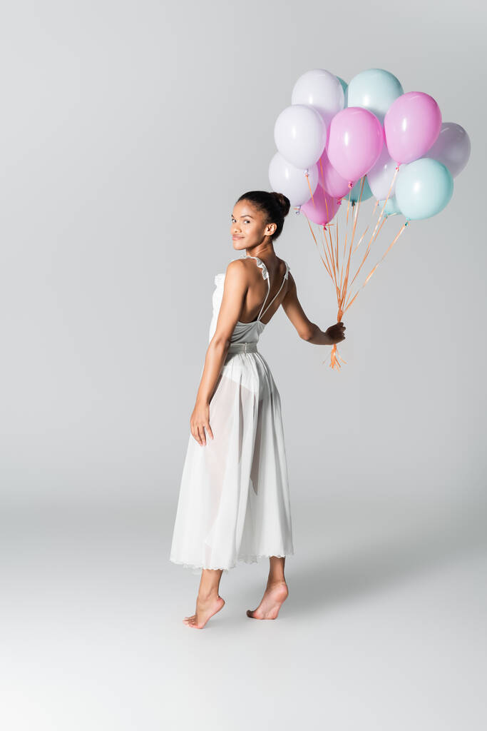 ξυπόλητη χαριτωμένη αφροαμερικάνικη μπαλαρίνα στο φόρεμα με μπαλόνια σε λευκό φόντο - Φωτογραφία, εικόνα