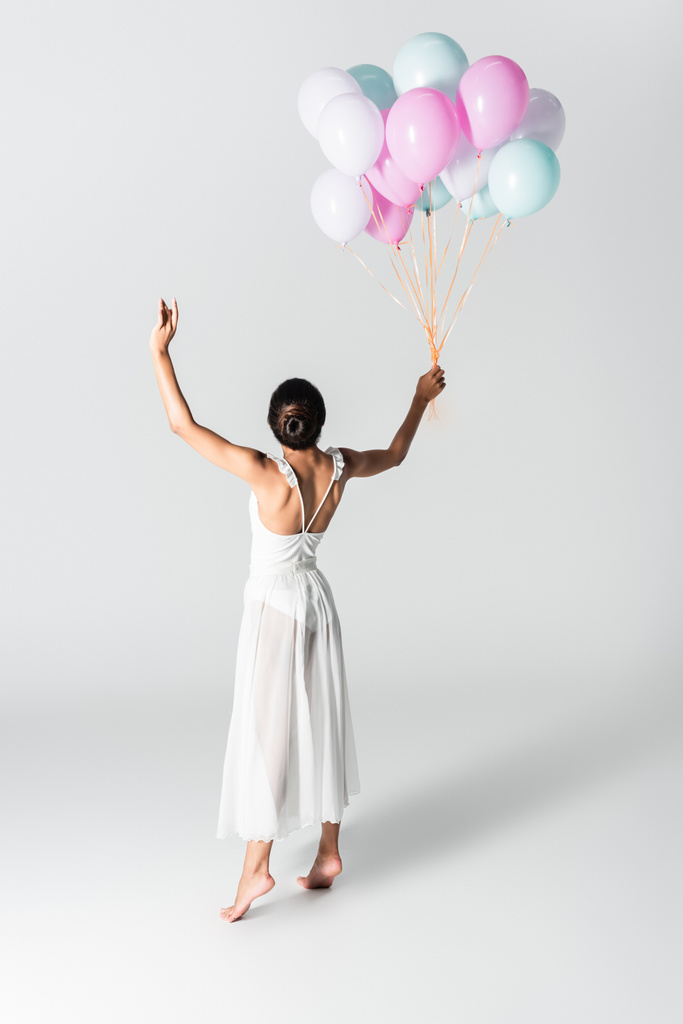 descalza elegante bailarina afroamericana en vestido bailando con globos sobre fondo blanco - Foto, imagen