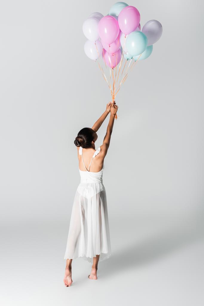 atrás vista de descalzo elegante bailarina afroamericana en vestido bailando con globos sobre fondo blanco - Foto, imagen