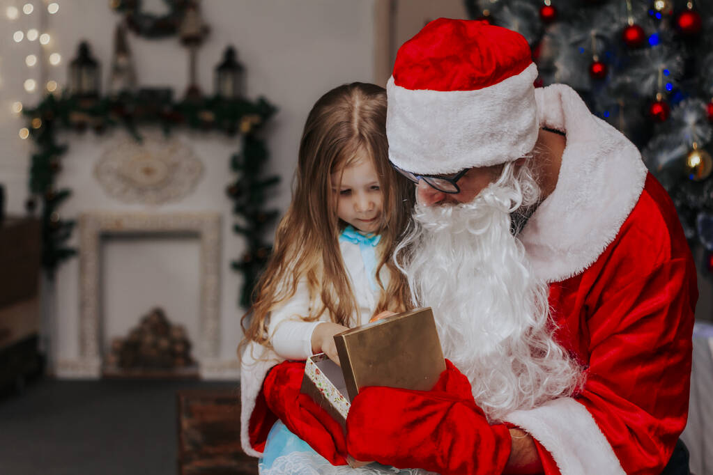 Άγιος Βασίλης άνοιγμα δώρο με χαριτωμένο κορίτσι μπροστά από το χριστουγεννιάτικο δέντρο  - Φωτογραφία, εικόνα