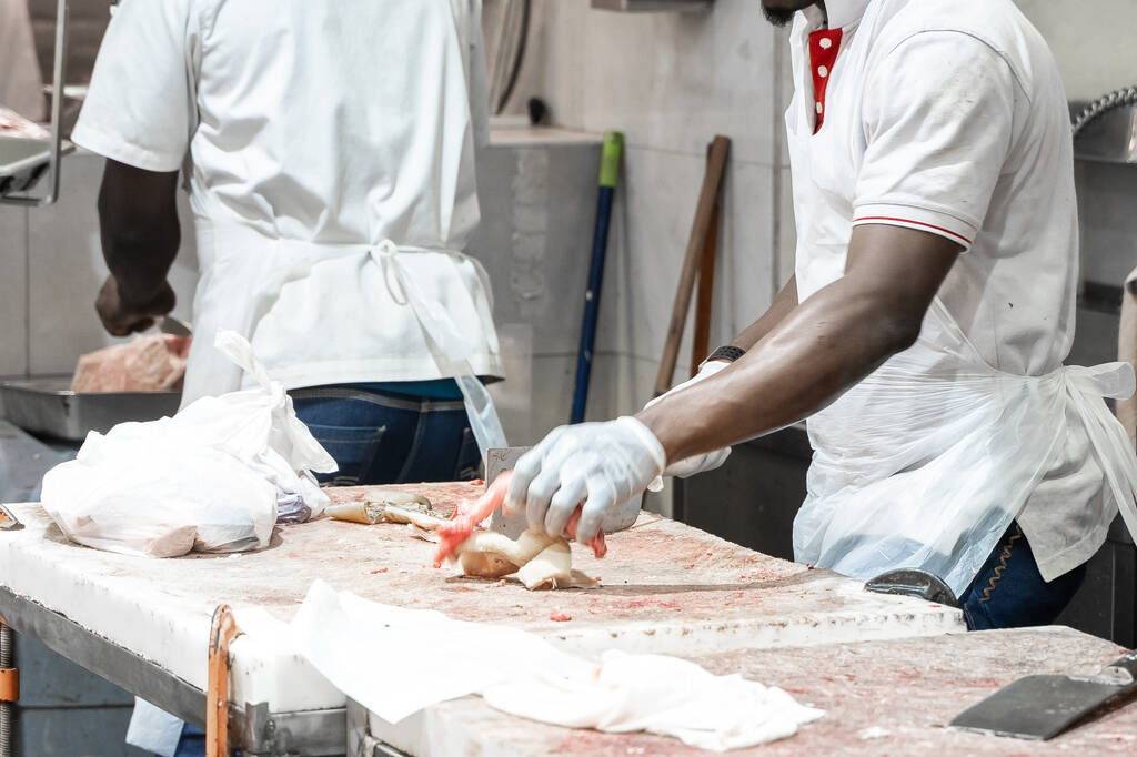Αφροαμερικάνος χασάπης κόβει κρέας στον πάγκο σε σφαγή. Ένας μάγειρας έκοψε φρέσκο κρέας μπέικον. - Φωτογραφία, εικόνα