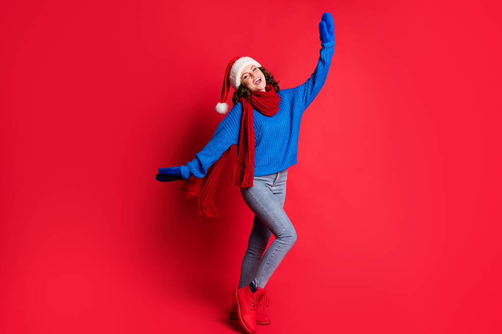 Foto retrato de chica alegre bailando tonteando alrededor animando posando extendiendo las manos brazos riendo usando pañuelo de jersey azul sombrero de santa aislado sobre fondo de color rojo brillante - Foto, Imagen
