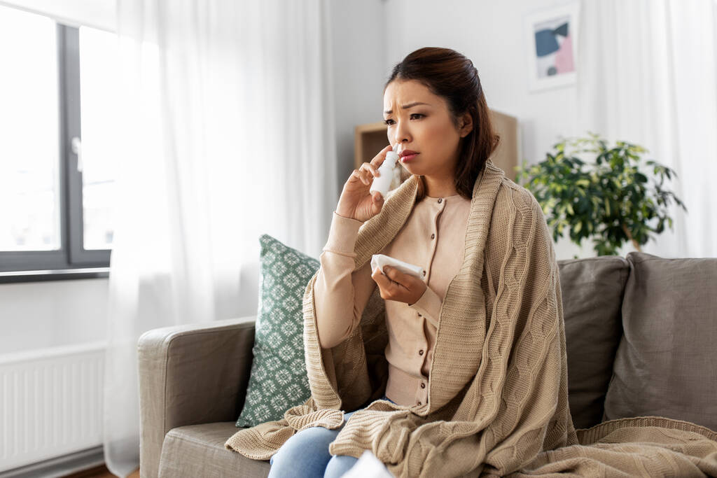 zieke aziatische vrouw met neusspray medicijn thuis - Foto, afbeelding