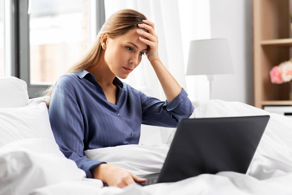 gestresste jonge vrouw met laptop in bed thuis - Foto, afbeelding