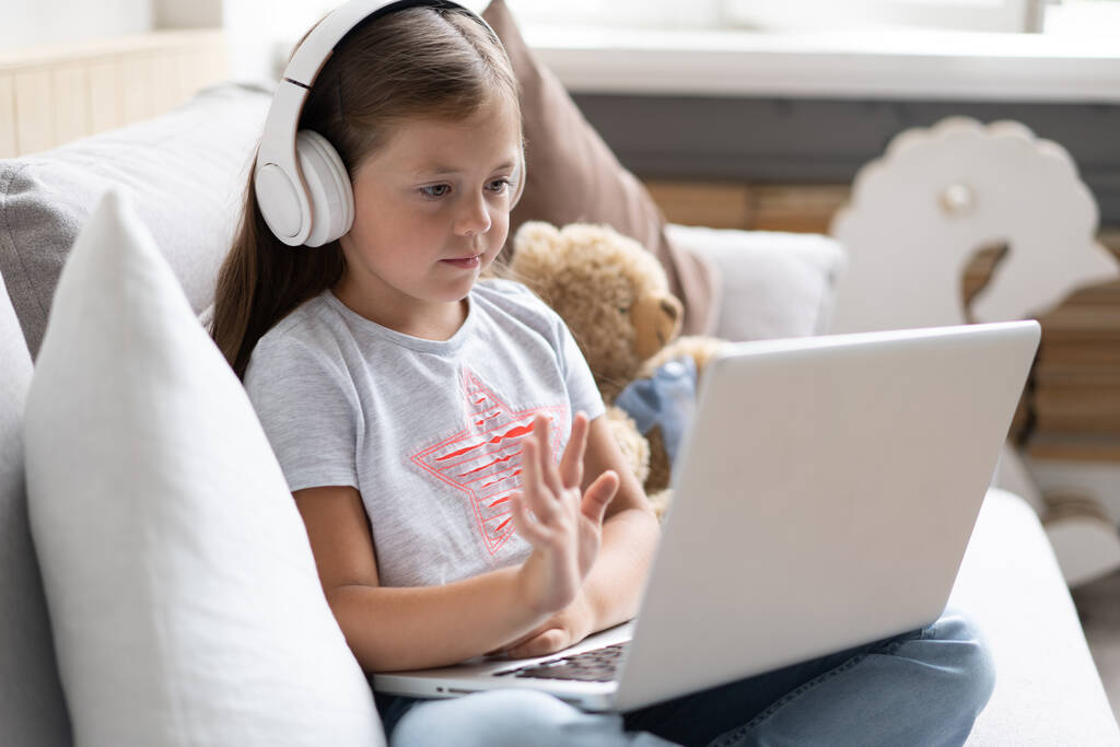 Онлайн-освіта. Солодка дівчина з навушниками дивиться відео урок вчителя конференції ноутбук, що сидить на дивані вдома
 - Фото, зображення