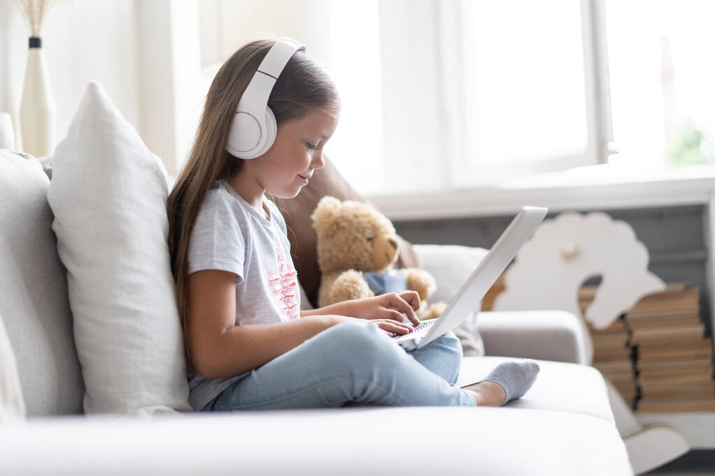 Online-koulutus. Sweet tyttö kuulokkeet näköinen video oppitunti opettaja konferenssi kannettava tietokone istuu sohvalla kotona - Valokuva, kuva