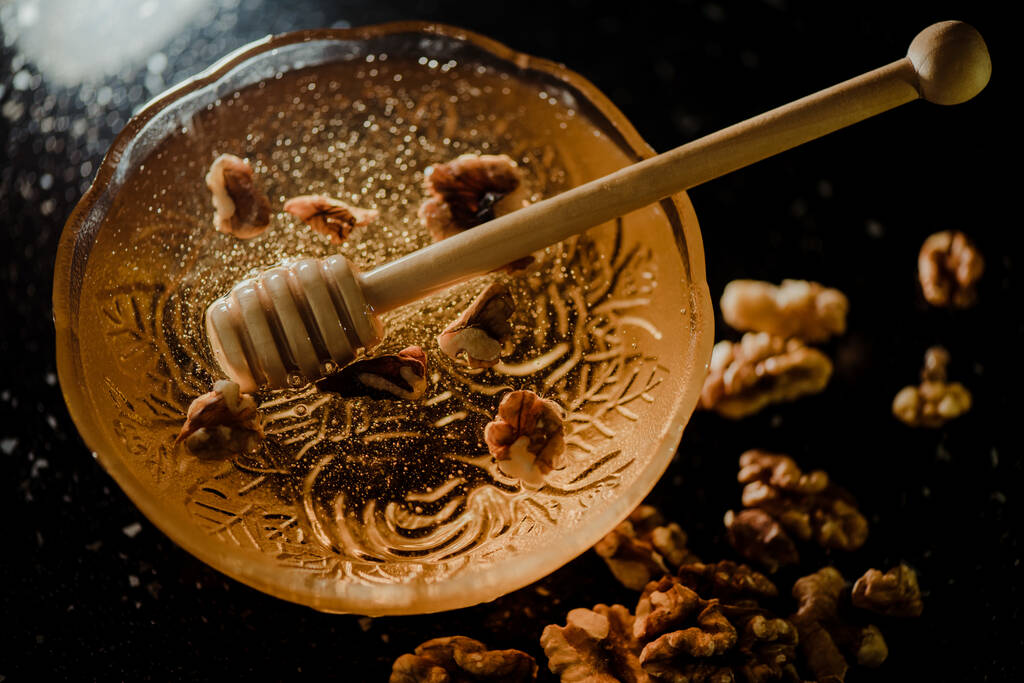 Wooden honey spoon dipped in a jar full of honey and nuts placed on a black background. Honey dripping around, pleasing and inviting photos. - Photo, Image