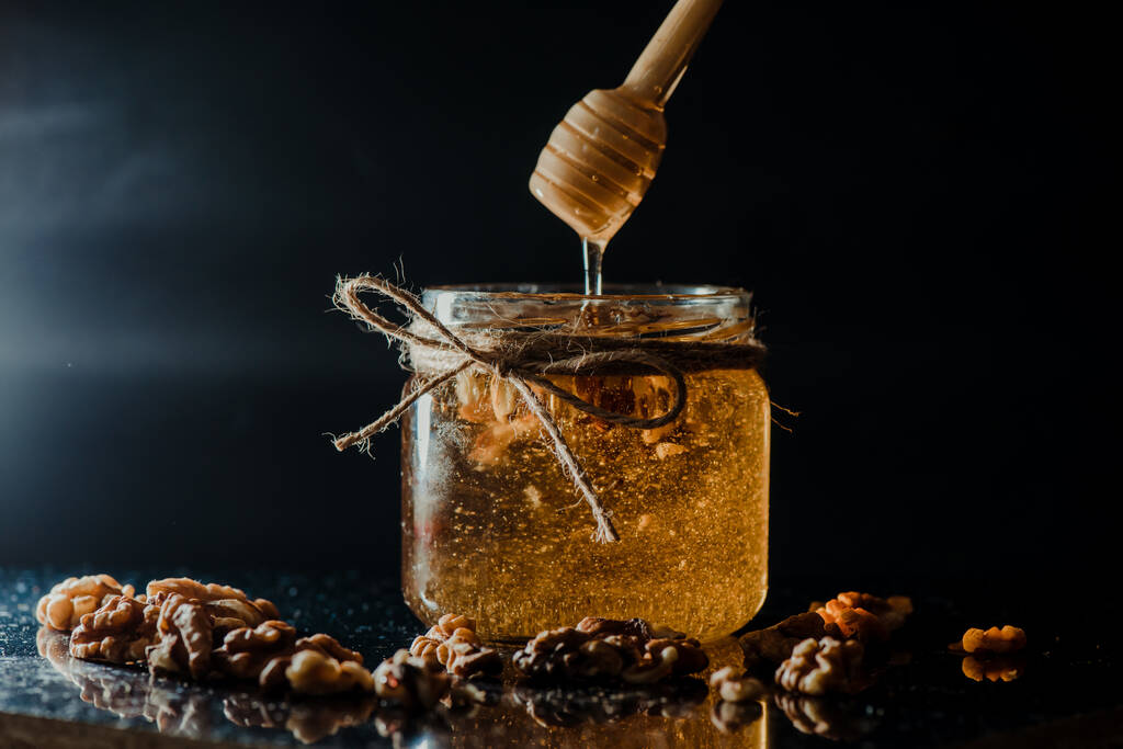 A méz egy üvegedényben dióval és fadobálóval. - Fotó, kép
