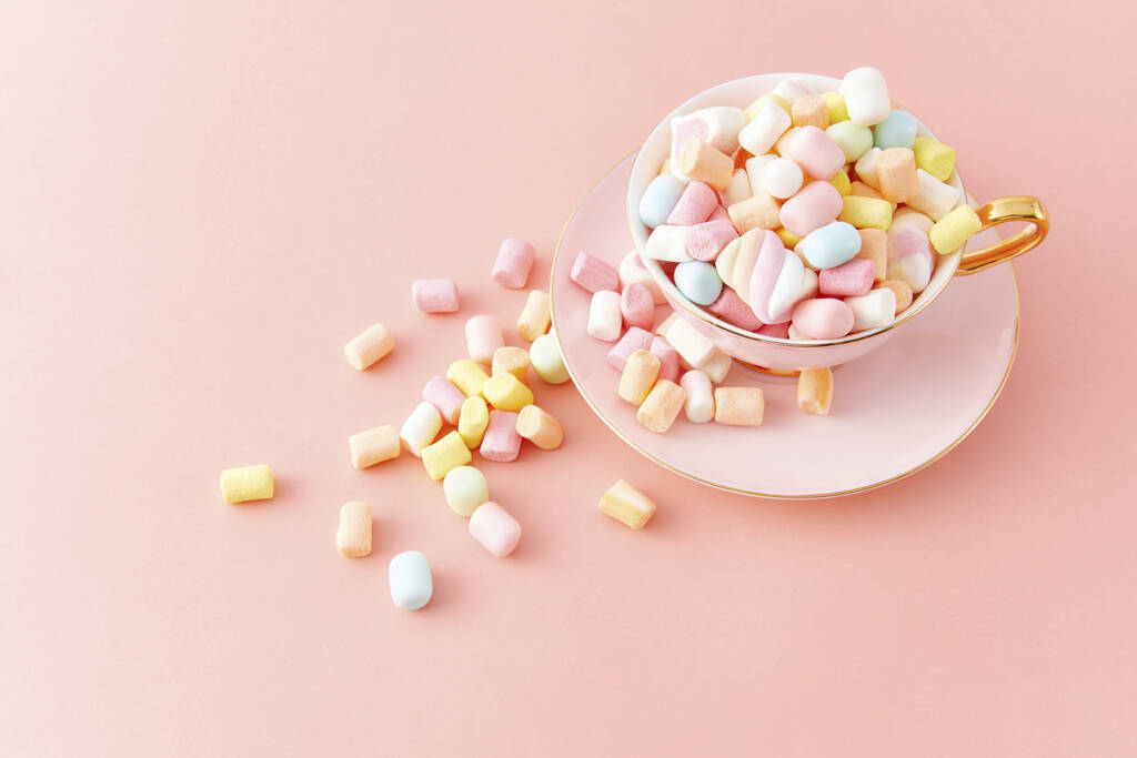 Un primo piano vista dall'alto di una tazza piena di marshmallow colorati isolati su uno sfondo rosa - Foto, immagini