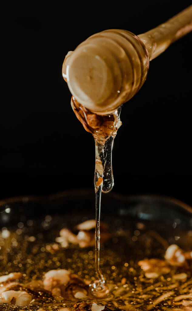 Cuillère à miel en bois trempée dans un bocal rempli de miel et de noix placé sur un fond noir. Miel dégoulinant, photos agréables et invitantes. - Photo, image