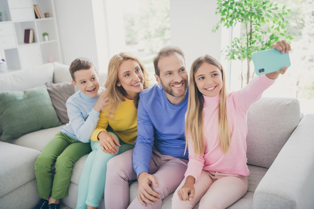 Foto de familia positiva personas mamá papá sentarse sofá niña hacer selfie en el teléfono inteligente en casa en el interior - Foto, imagen