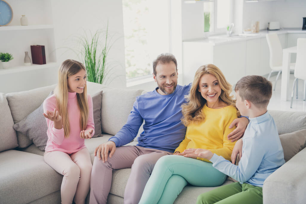 Photo of positive cheerful two kids boy girl sit couch tell mom dad news in house indoors - Photo, Image