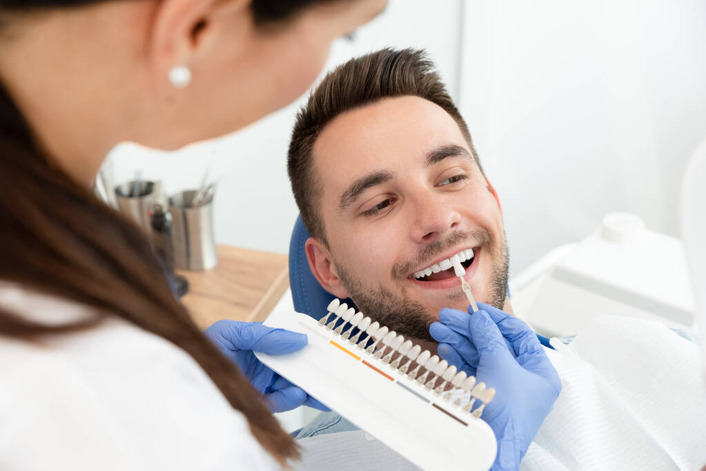 Красивий молодий чоловік у стоматологічній клініці з жінкою-стоматологом. Відбілювання здорових зубів
. - Фото, зображення