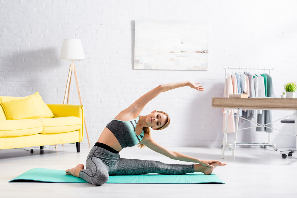 Deportiva estirándose en colchoneta de fitness mientras practica yoga en casa  - Foto, Imagen