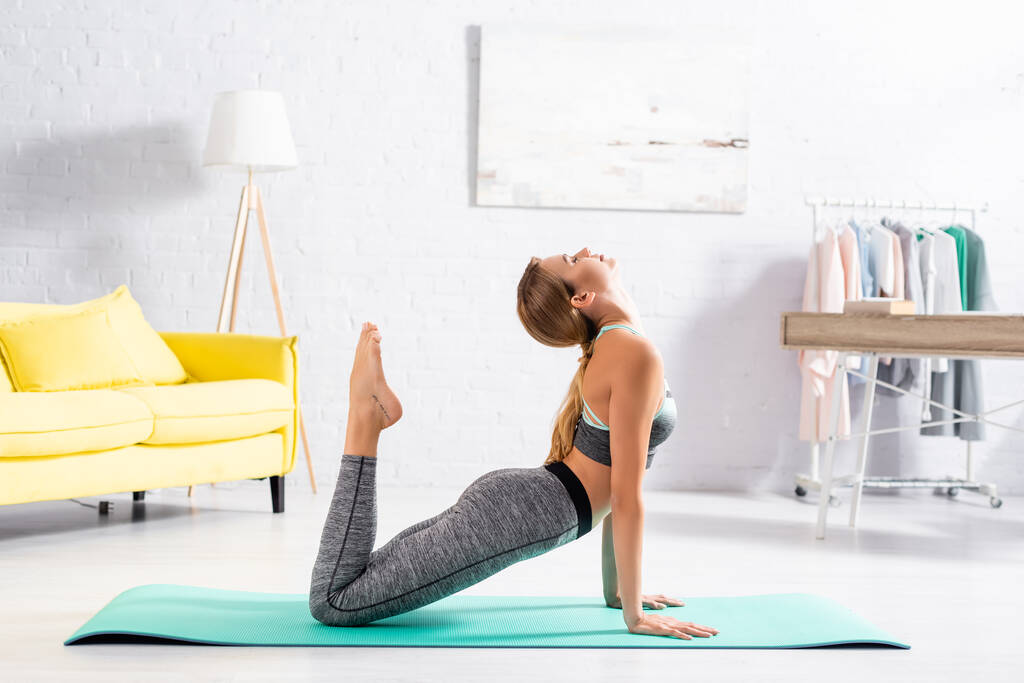 Seitenansicht einer jungen Frau mit geschlossenen Augen, die zu Hause Yoga praktiziert  - Foto, Bild