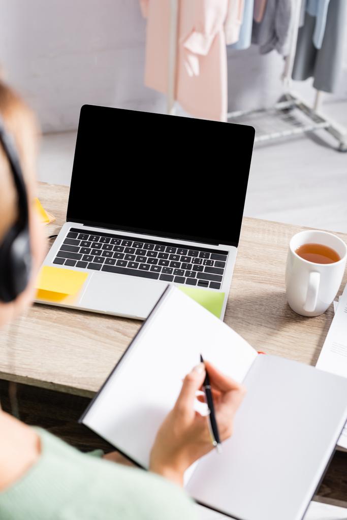 Laptop üres képernyőn közel csésze tea és szabadúszó headset írás notebook elmosódott előtérben   - Fotó, kép