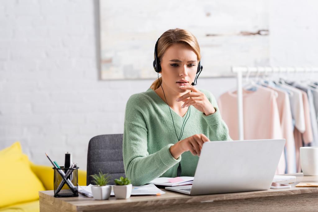 Blondynka freelancer w słuchawkach mając wideo czat na laptopie na rozmytym pierwszym planie  - Zdjęcie, obraz