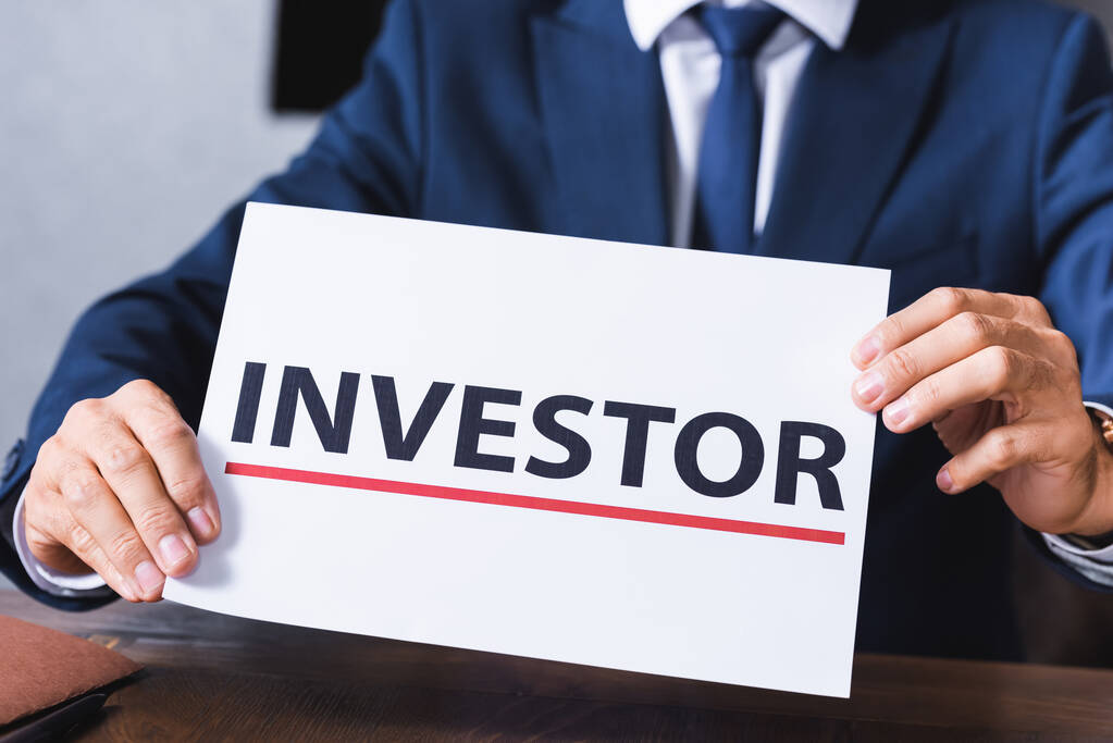 Ausgeschnittene Ansicht eines Geschäftsmannes mit einem Schild mit Investorenaufdruck im Besprechungsraum auf verschwommenem Hintergrund - Foto, Bild
