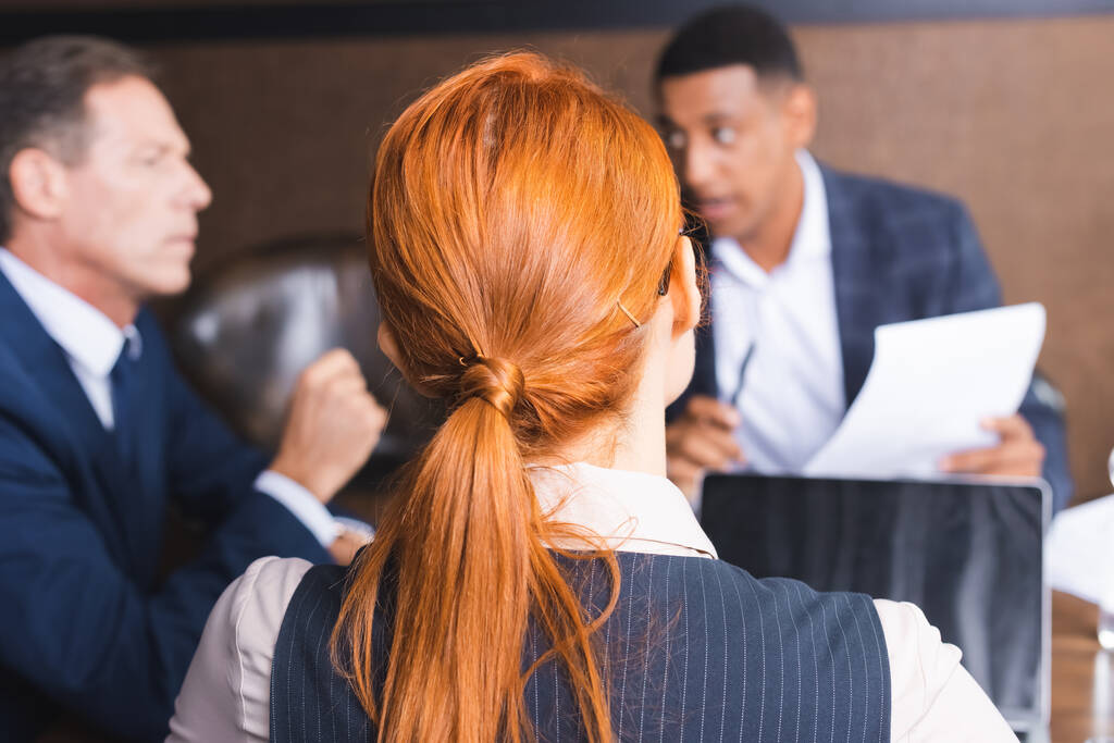 Vissza kilátás vörös hajú üzletasszony elmosódott kollégák megvitatása a háttérben tárgyalóteremben - Fotó, kép