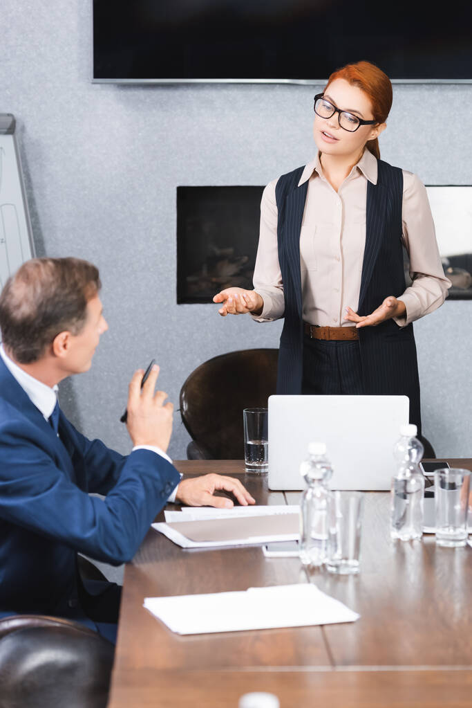 Gestos ejecutivos femeninos mientras habla con una colega sentada en el lugar de trabajo durante una reunión de negocios - Foto, imagen