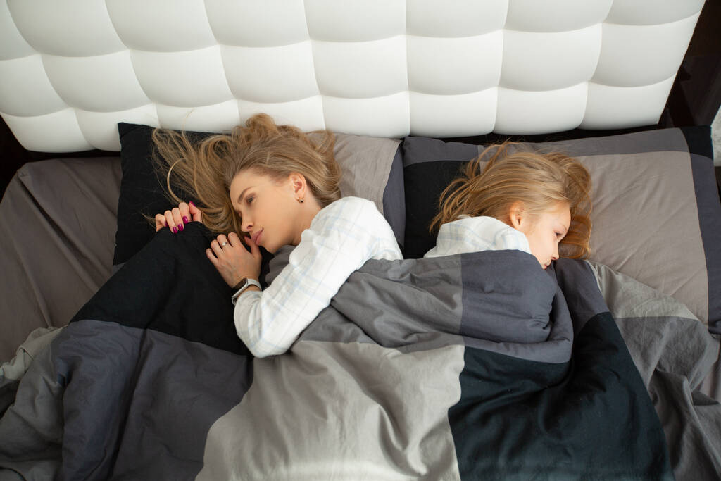 beautiful mom and daughter lie on the bed under the covers - Photo, Image