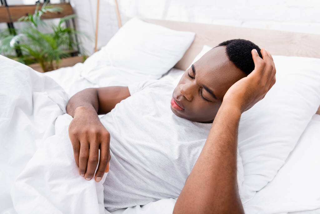 Afroamerikaner berührt Kopf, während er auf Bett liegt  - Foto, Bild