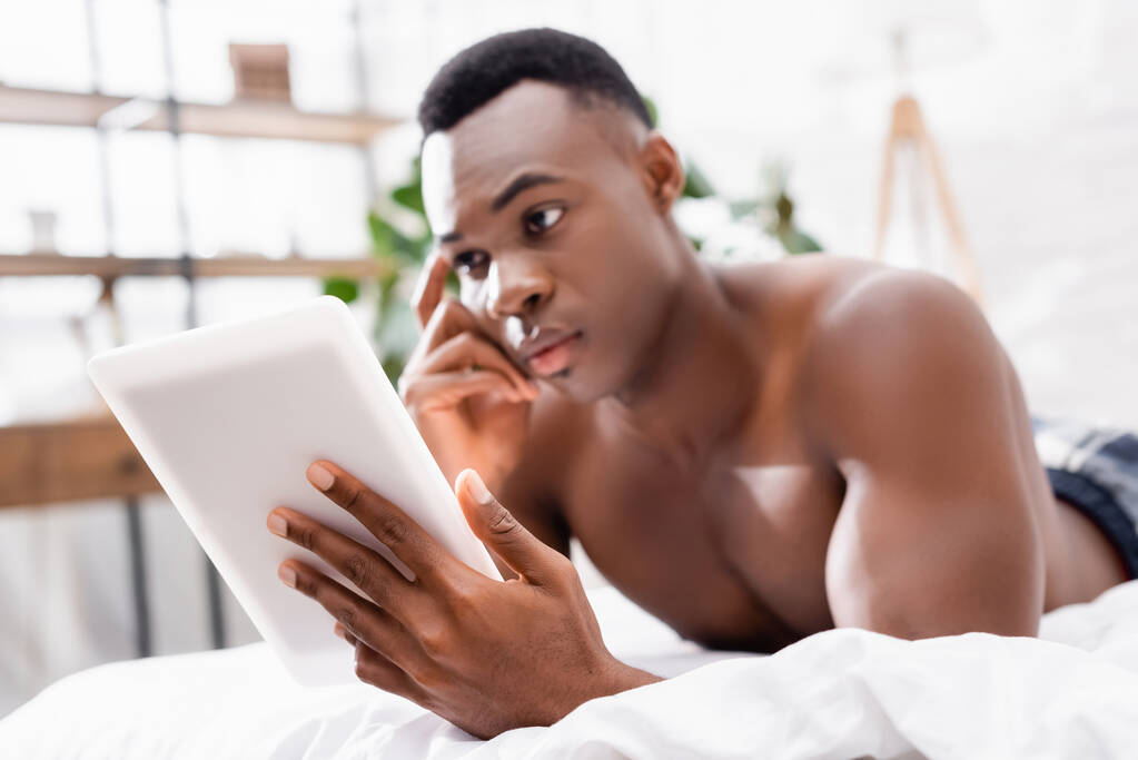 Tablet digital na mão de homem americano africano na cama sobre fundo borrado  - Foto, Imagem